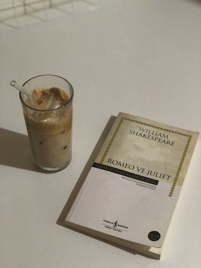 Chilled iced coffee alongside Shakespeare's Romeo and Juliet book on a table.